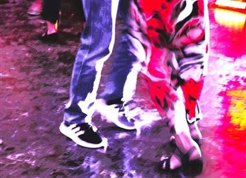 Two people are dancing on a shiny surface. Their legs are in motion and there is colorful lighting in the background.