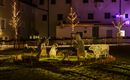 Eine beleuchtete Weihnachtskrippe aus Drahtfiguren zeigt eine Szene mit Tieren und Menschen. Die Installation ist nachts sichtbar und umgeben von festlicher Beleuchtung.
