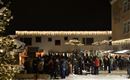 Ein belebter Weihnachtsmarkt mit festlicher Beleuchtung in der Nacht. Menschen versammeln sich in einer winterlichen Atmosphäre.