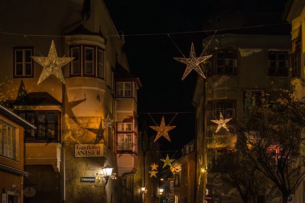 Eine festlich beleuchtete Straße mit großen Sternen, die zwischen den Gebäuden hängen. Die Atmosphäre ist gemütlich und einladend.