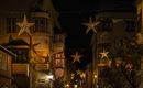 Eine festlich beleuchtete Straße mit großen Sternen, die zwischen den Gebäuden hängen. Die Atmosphäre ist gemütlich und einladend.