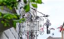 Ein traditionelles Schild eines Gasthauses hängt an einem Gebäude. Im Hintergrund ist ein klarer Himmel und grüne Blätter zu sehen.
