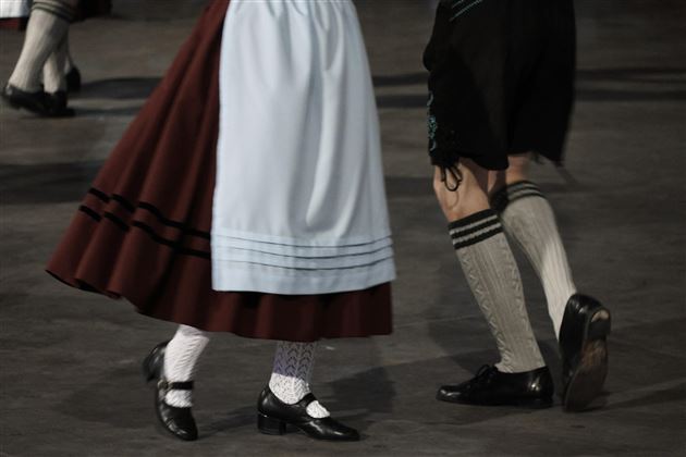 Dancing people in traditional clothing. A red skirt and black shoes can be seen.