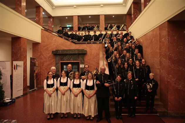 Un grande gruppo di musicisti è in piedi su una scala elegante. Indossano uniformi festose e abiti tradizionali tedeschi.