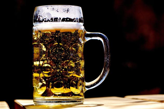 Een bierpul met schuimend, gouden vloeistof staat op een tafel. Het glas is helder en de belletjes zijn zichtbaar.