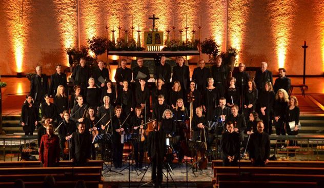 Een gemengd koor staat in een kerk en zingt. De ruimte is feestelijk versierd met zacht licht en decoratieve elementen.