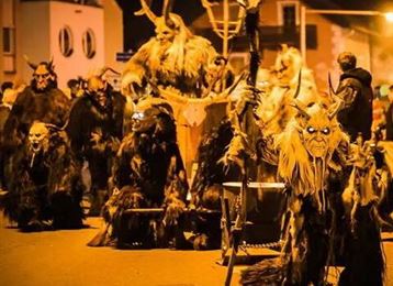 Un gruppo di persone in costumi e maschere inquietanti, che si trovano in una strada. La scena è di notte e illuminata da una luce soffusa.