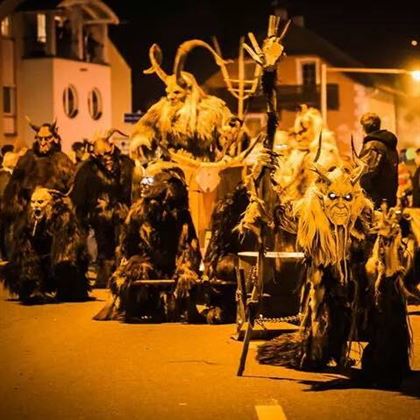 Un groupe de personnes en costumes et masques sinistres se tient dans une rue. La scène est de nuit et éclairée faiblement.