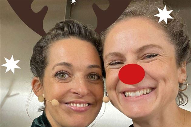 Two people are sitting on boxes and looking at a large tree made of paper. The scene is well-lit and conveys a creative atmosphere.