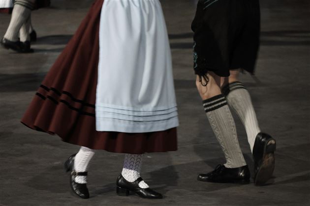 Tanzende Personen in traditioneller Kleidung. Die Füsse sind in Bewegung, umgeben von einer festlichen Atmosphäre.