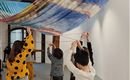 Eine Gruppe von Kindern zieht an bunten Tüchern in einem Ausstellungsraum. Die Atmosphäre ist kreativ und spielerisch.