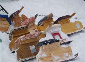 Een verzameling sleetjes ligt in de sneeuw. De sleetjes zijn van hout en in verschillende kleuren.