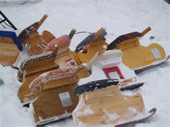 Eine Ansammlung von Schlitten liegt im Schnee. Die Schlitten sind aus Holz und in verschiedenen Farben.