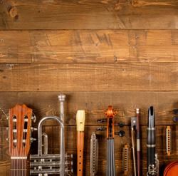 Een selectie van muziekinstrumenten op een houten tafel. Daaronder zijn een gitaar, trompet, blokfluit, viool en verschillende houten blaasinstrumenten.