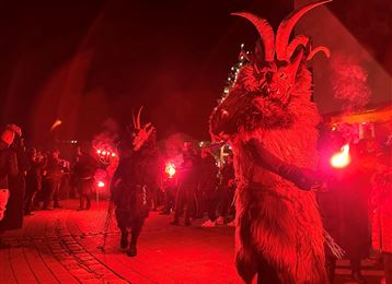 Un evento notturno con persone decorate in costumi di pelliccia e maschere. Portano torce e si circondano di una folla contemplativa.