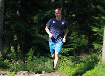 Ein Mann joggt auf einem Waldweg. Um ihn herum sind grüne Bäume und viele Pflanzen.