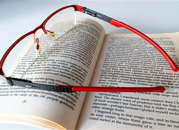 Un occhiale si trova su un libro aperto. Le pagine sono stampate con del testo e gli occhiali sono rossi e moderni.