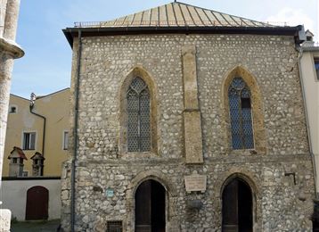 Ein historisches Gebäude aus Stein mit gotischen Fenstern. Die Fassade zeigt eine interessante Architektur und befindet sich in einer ruhigen Umgebung.