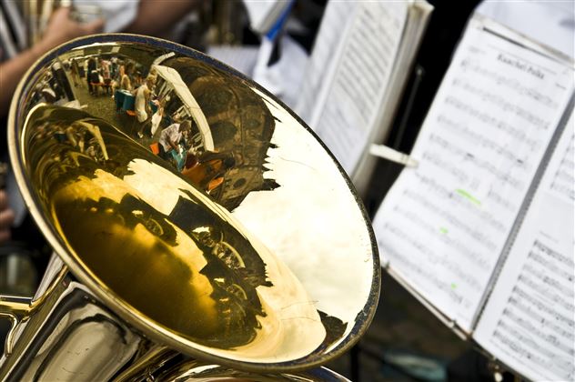 Ein glänzendes Tuba mit reflektierenden Bildern von Menschen. Im Hintergrund sind Notenblätter zu sehen.