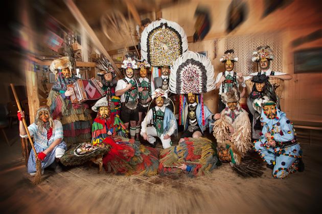 Eine Gruppe von Menschen in traditionellen Kostümen steht in einem Raum. Sie tragen aufwendige Kopfstücke und stellen eine kulturelle Zeremonie dar.