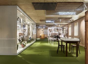 Een modern en licht kantoor met een groene vloerbedekking. De ruimtes zijn uitgerust met planken en tafels voor samenwerking.