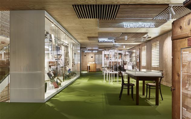 Un bureau moderne et lumineux avec une surface de moquette verte. Les pièces sont équipées d'étagères et de tables pour la collaboration.