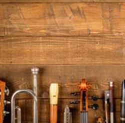 A collection of musical instruments on a wooden table. Among them are various string instruments, wind instruments, and woodwind instruments.