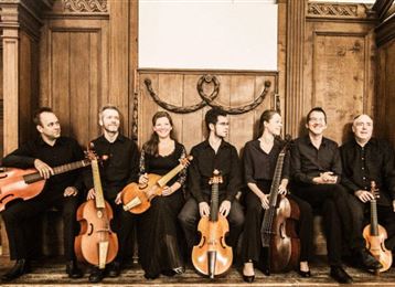 Een groep muzikanten zit in elegante kleding in een historische ruimte. Ze houden verschillende instrumenten vast en stralen een muzikale sfeer uit.