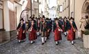 Eine Gruppe von Menschen in traditioneller Kleidung marschiert durch eine enge Straße. Sie tragen historische Trachten und Hüte und scheinen an einer Festlichkeit teilzunehmen.