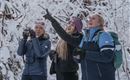 Drei Frauen stehen im Schnee und schauen nach oben. Sie lachen und wirken begeistert von der winterlichen Landschaft.