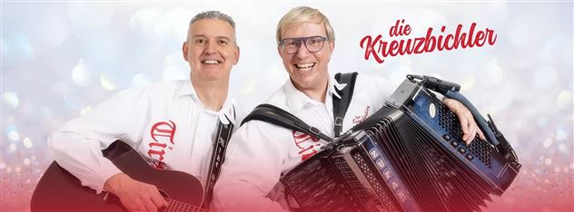 Zwei Musiker lächeln in die Kamera. Der eine spielt Gitarre und der andere ein Akkordeon.