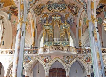 Un'imponente decorazione interna di una chiesa con un grande organo in primo piano. Le pareti sono artisticamente decorate con affreschi ed elementi decorativi.
