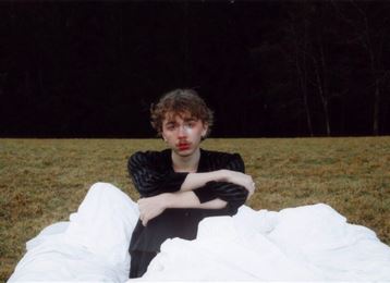 A young man sits casually on a green sofa. Above him hangs an elegant lamp that creates a cozy atmosphere.
