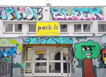 Una casa per giovani con graffiti colorati sulla facciata. Sopra l'ingresso c'è scritto "park in" e "Hip Hop Block" in colori vivaci.