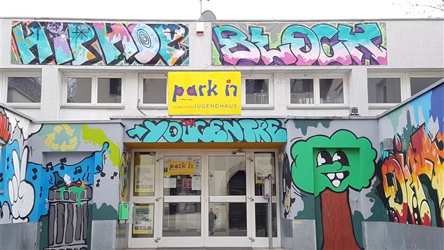Una casa per giovani con graffiti colorati sulla facciata. Sopra l'ingresso c'è scritto "park in" e "Hip Hop Block" in colori vivaci.