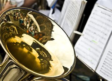 A shiny tuba with reflective details in metal. Sheet music is visible in the background.