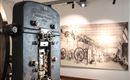 Eine alte Maschine in einem Museum, die die industrielle Geschichte symbolisiert. Im Hintergrund ist eine historische Zeichnung einer Fabrik zu sehen.