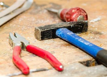 Une banque de travail avec différents outils. On peut voir une pince, un marteau et des copeaux de bois.