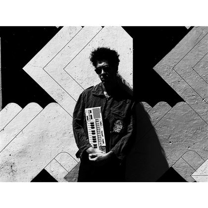 A man stands in front of a graphic wall and holds a keyboard in his hands. The scene is in black and white and conveys an artistic impression.