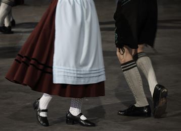 Traditional clothing and dances from a folkloric performance. The legs of dancers in colorful costumes are visible.