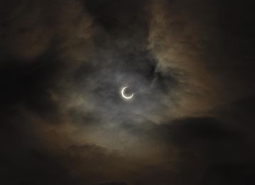 Ein dunkler Himmel mit Wolken und einer teilweisen Mondfinsternis. Der Mond erscheint schmal und strahlt schwaches Licht aus.