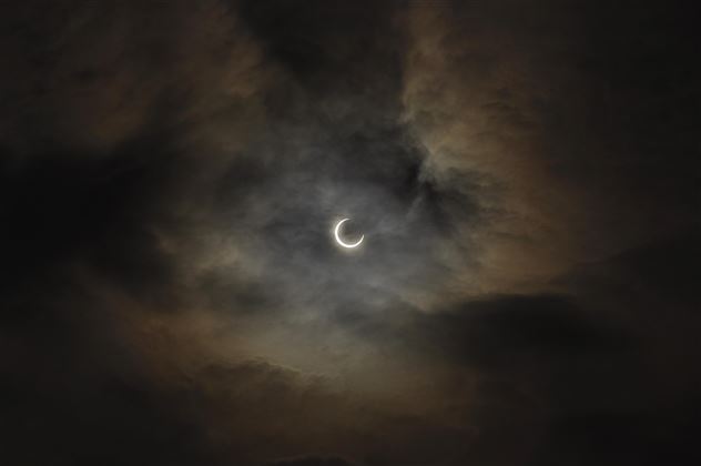 Ein dunkler Himmel mit Wolken und einer teilweisen Mondfinsternis. Der Mond erscheint schmal und strahlt schwaches Licht aus.