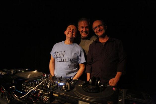 A person is relaxing in a lounge chair with headphones. In the background, green plants and tables are visible.