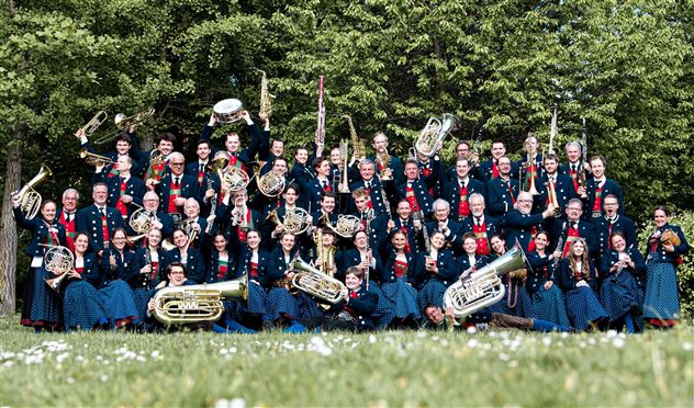 Un grand groupe de musiciens se tient à l'extérieur et tient divers instruments à vent. Ils portent des vêtements uniformes et sourient à la caméra.