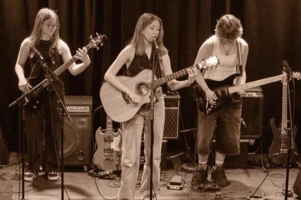 Un groupe se produit sur scène. Les musiciennes jouent de la guitare et de la basse dans une pièce tamisée avec des lumières colorées.