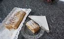 Une strudel aux pommes fraîchement sorti du four sur une assiette blanche. À côté, se trouve un morceau de strudel sur une assiette en verre.