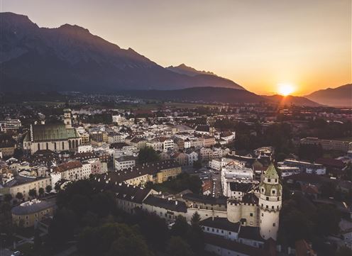Eine atemberaubende Stadtansicht bei Sonnenuntergang, umgeben von Bergen. Das Bild zeigt historische Gebäude und einen klaren Himmel.