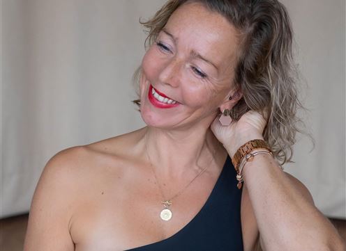 A smiling woman with curly hair is wearing a black top. She sits relaxed and appears friendly.