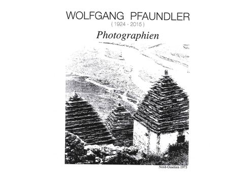 Eine Schwarzweißaufnahme von traditioneller Architektur mit geschlossenen Dächern aus Schindeln. Im Hintergrund sind Hügel und eine ländliche Landschaft sichtbar.