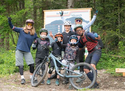 Eine Gruppe von sechs Personen in Radfahrkleidung steht in einem Waldgebiet. Sie posieren neben einem Mountainbike und haben Spaß.